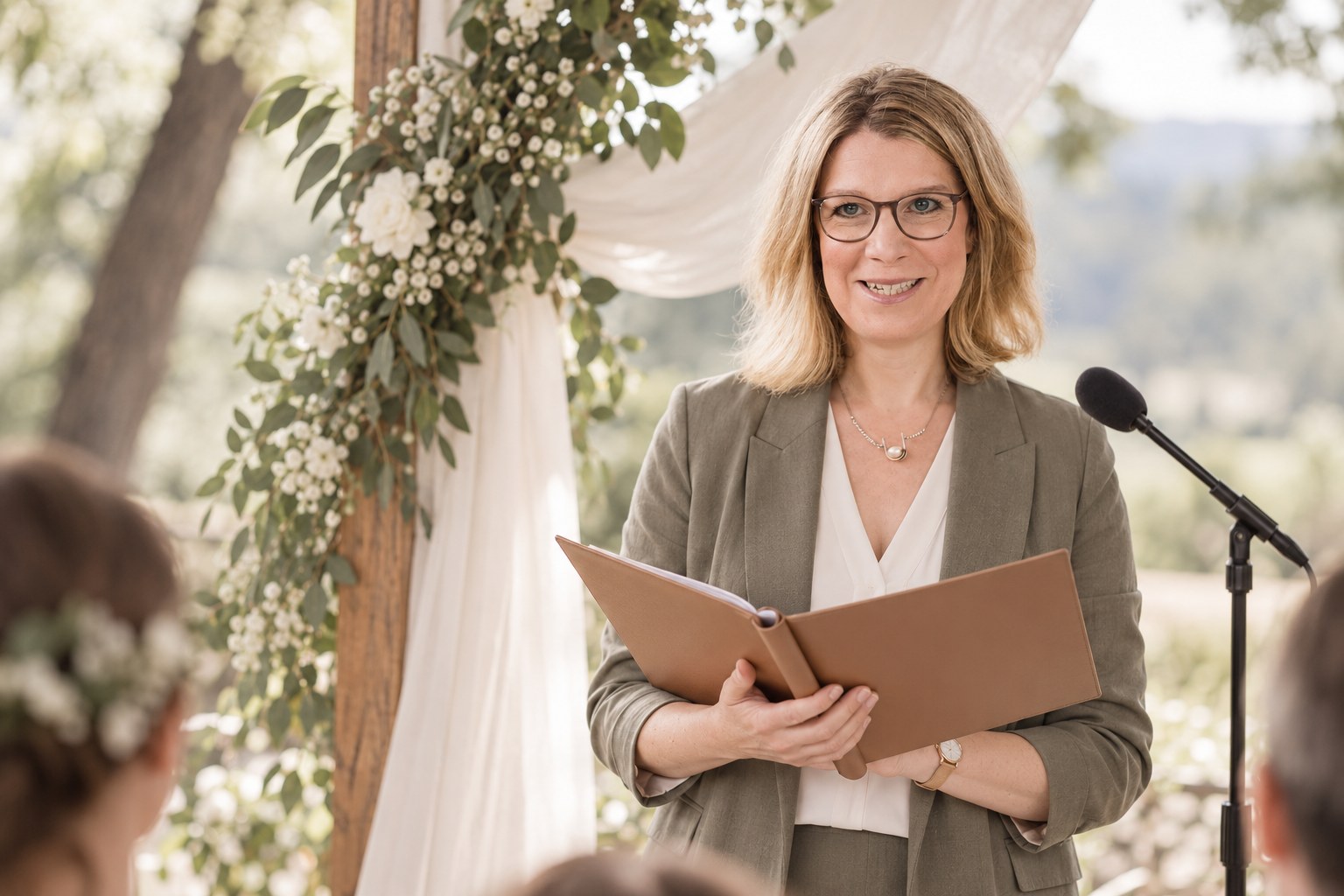 erste Traurede 2027. KI-generierte Darstellung von Anja Happe mit geöffneter Redemappe neben einem Mikrofon unter einem blumengeschmückten Traubogen.